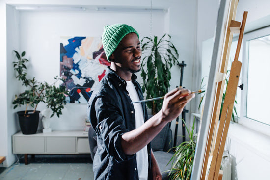 A young black man is painting in an art studio.