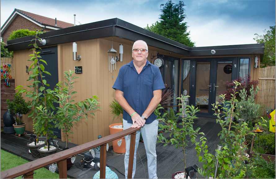 A man standing in front of a garden shed.