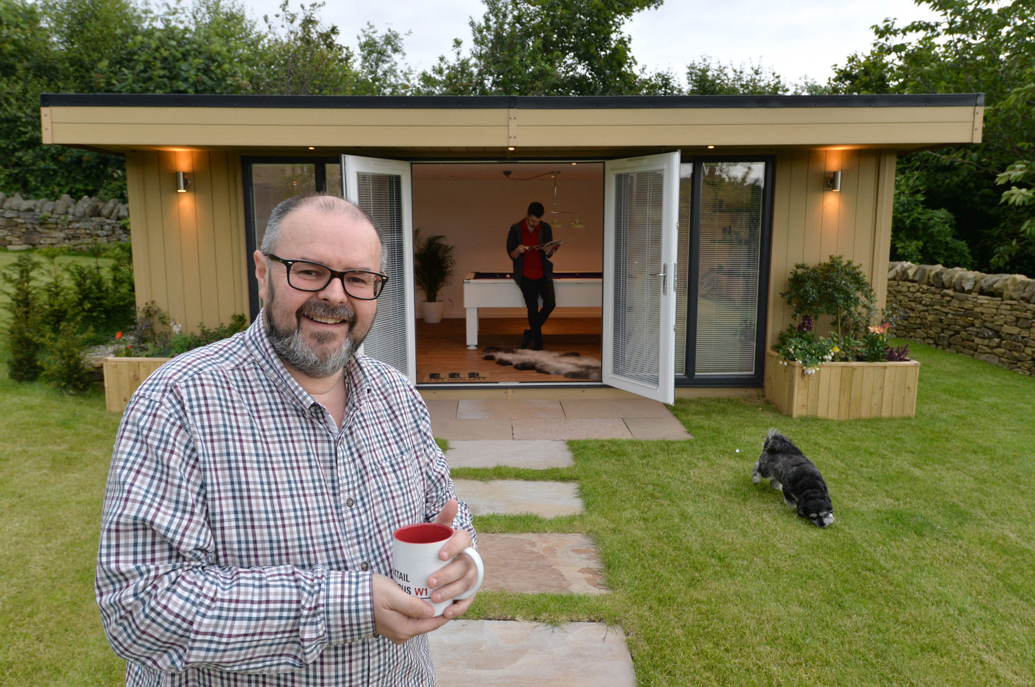 A man standing in front of a shed with a cup of coffee.