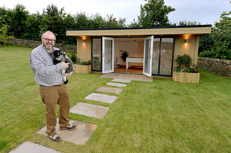 A man holding a dog in front of a house.