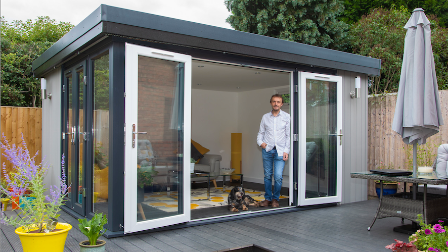 A man standing in front of a garden shed.