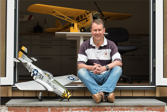 A man sits on the steps of his garden room in wilmslow with a model airplane, as part of his garden room workshop.