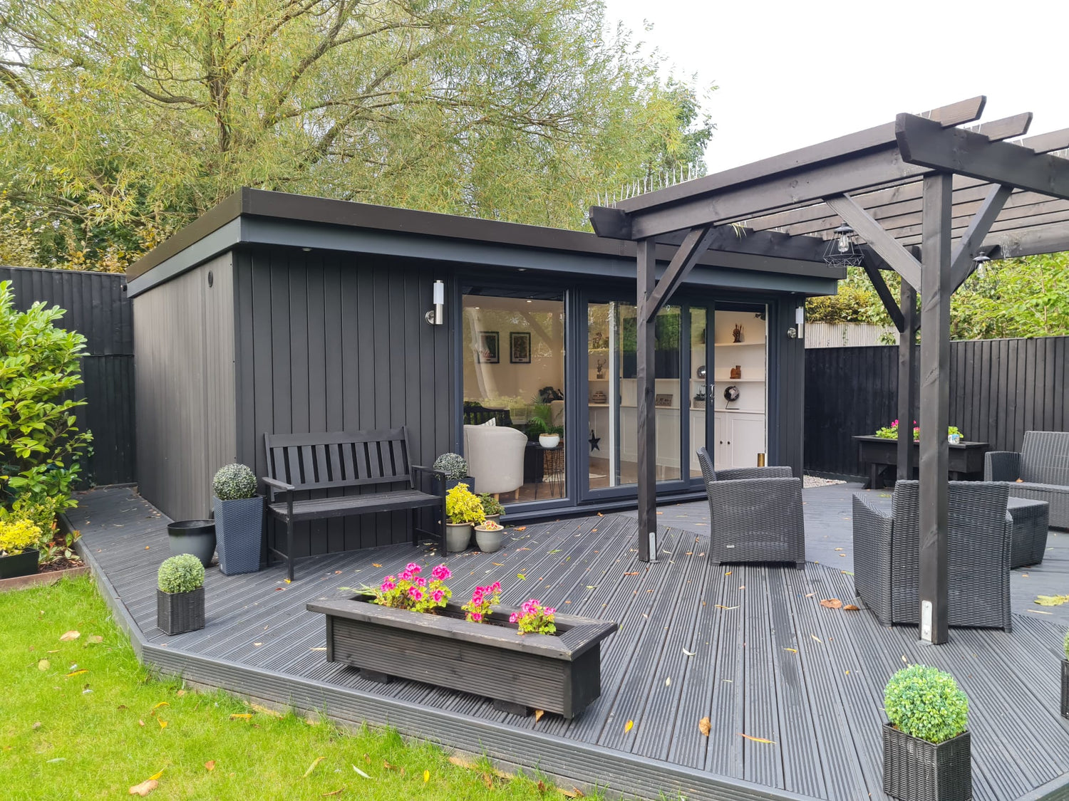 A black garden shed with a wooden deck.