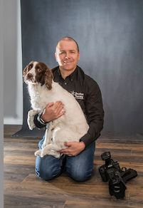A man posing with his dog in front of a camera.