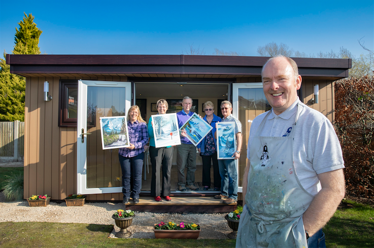 A garden room office in Chester with people standing showing their artwork .