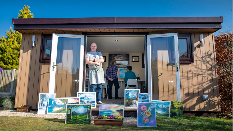 A man standing in front of a shed with paintings.