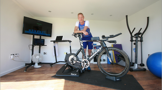 A great british triathlete standing next to an exercise bike in a rubicon garden room.