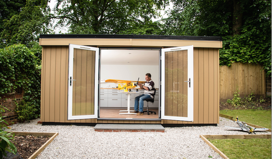 A man is working on a model airplane in a garden shed.