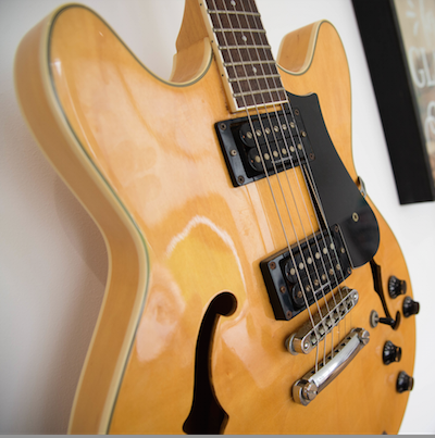 A yellow electric guitar is hanging on a wall.