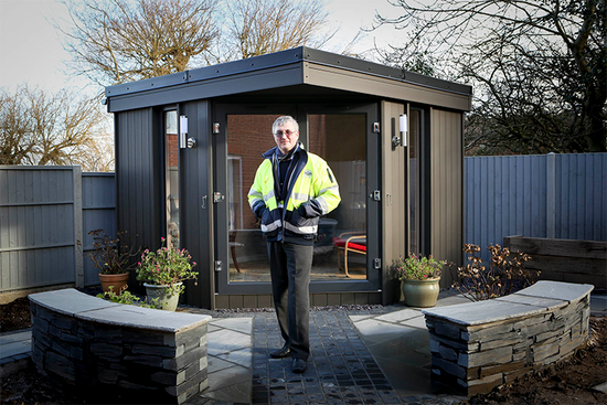 A man standing in front of a small shed.