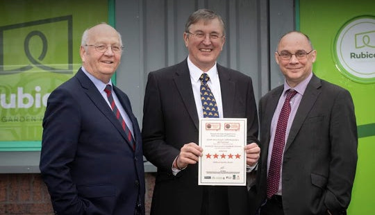 Three men standing in front of a building holding a certificate.