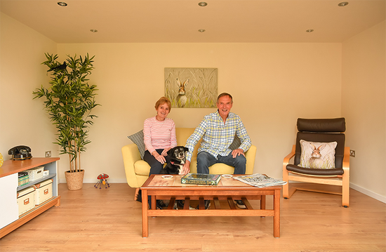 A man and woman sitting on a couch in a rubicon garden room, which is used as a living room.