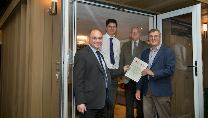 Three men standing in front of a door with a certificate.